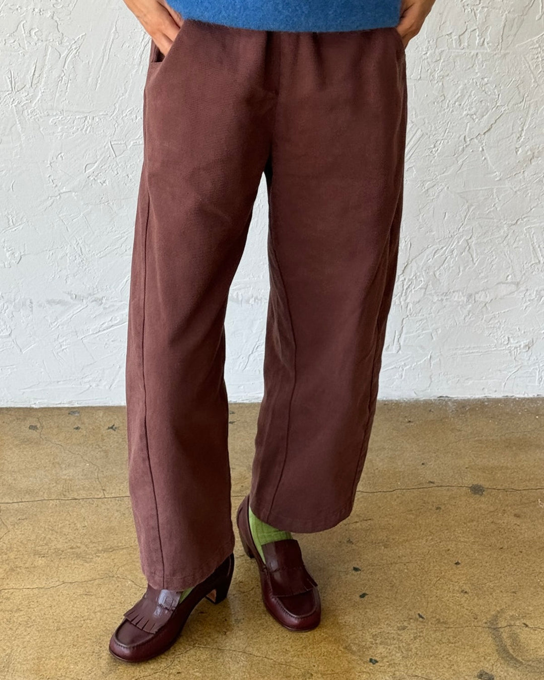 Person wearing brown pants and a blue top against a white wall.